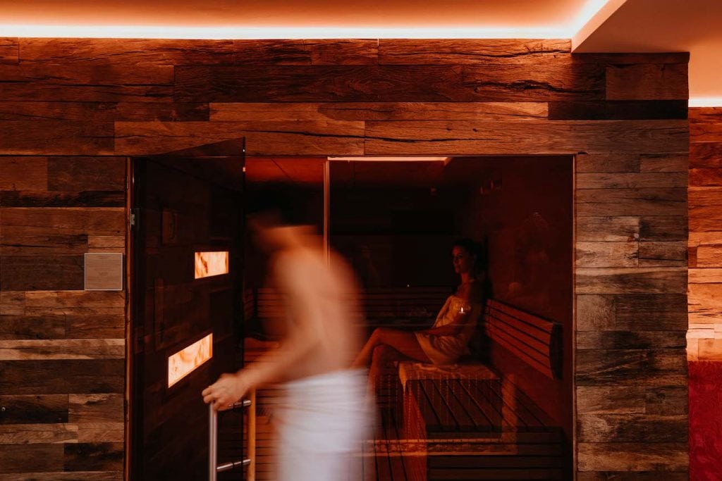 Frau genießt in Sauna, ein Mann läuft vorbei