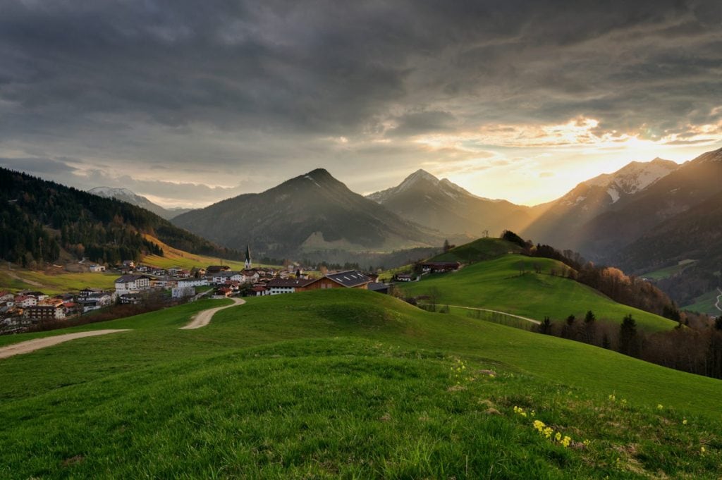 Sonnenschein mit bedecktem Himmel auf einer Wiese in Tirol mit Bergblick