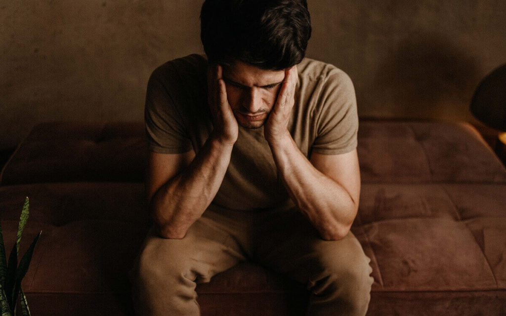 Epigenetisches Mind Detox im Ayurveda Mann sitzt mit dem Kopf in die Hände gestützt vor einem dunklen Hintergrund