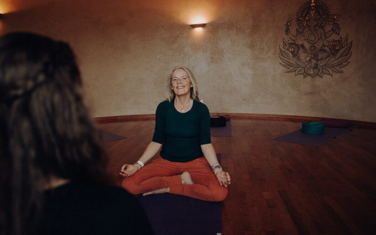 Longevity im European ayurveda; ältere Frau mit roter Hose sitzt im Lotossitz auf dem Boden