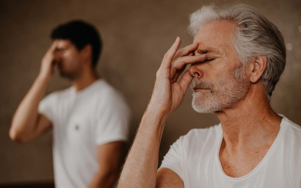 Pranayama für Ojas: Ein Mann atmet bewusst, dabei hält er mit einer Hand ein Nasenloch zu